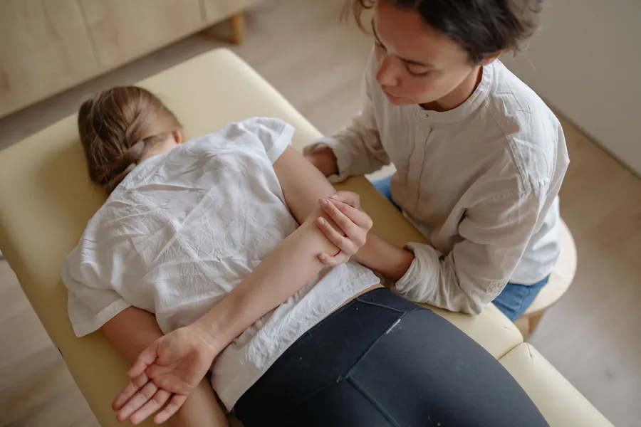 A chiropractor works on a patient's shoulder and upper back as she lies face down on a treatment table