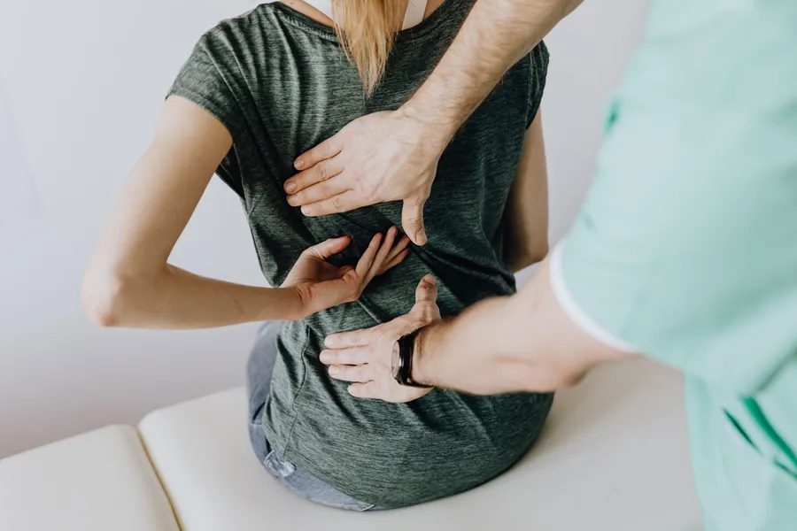A patient seated on an exam table points to her low back while a clinician checks the spot